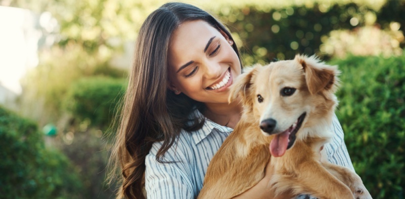 Woman smiling and holding a dog in a garden