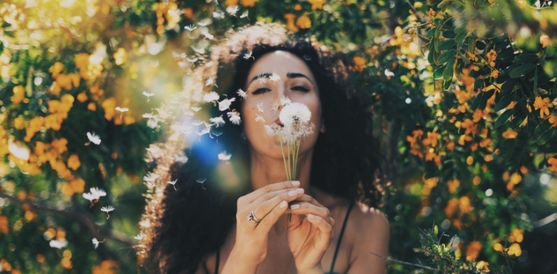 Woman blowing a dandelion clock in a field of flowers