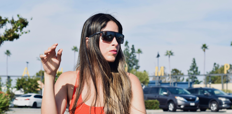 A young woman wearing a pair of Oakley sunglasses in a parking lot.